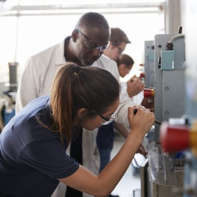 Engineer training female apprentice using a drill press